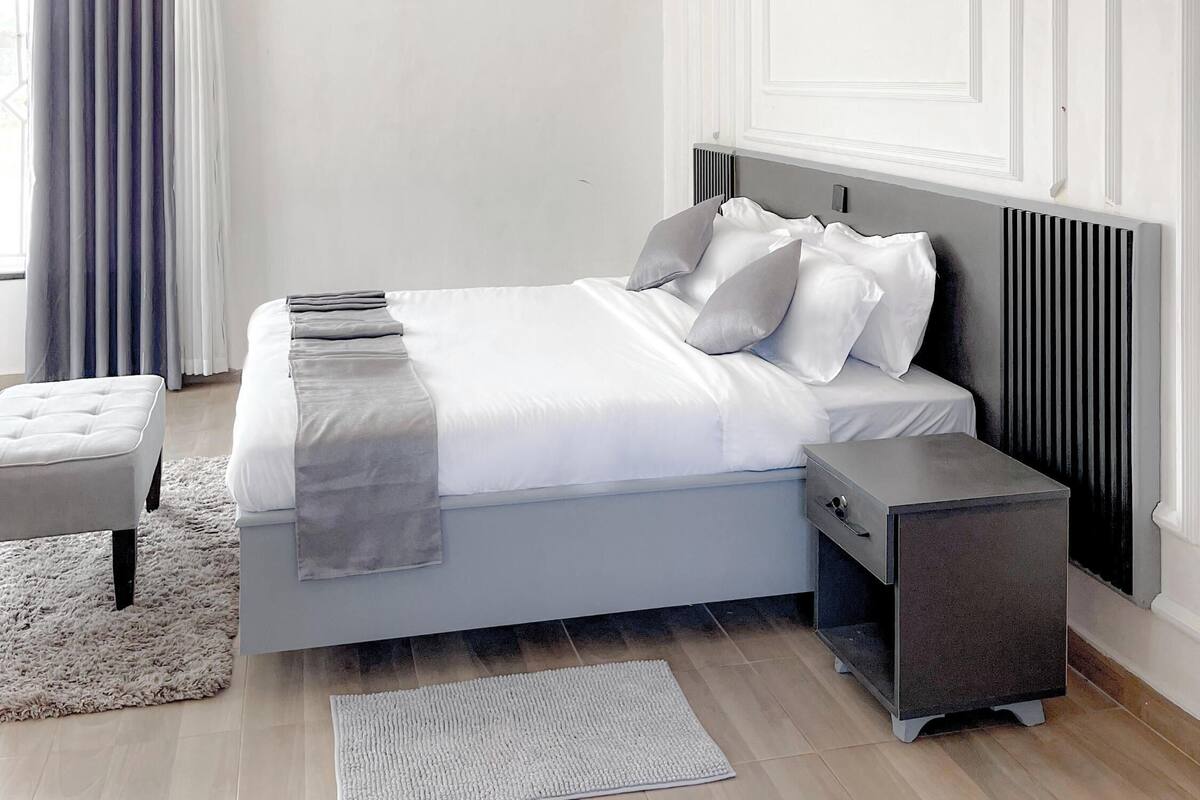 Een moderne slaapkamer met een bed, nachtkastjes, een vloerkleed in een lichte kleur en een raam met gordijnen.