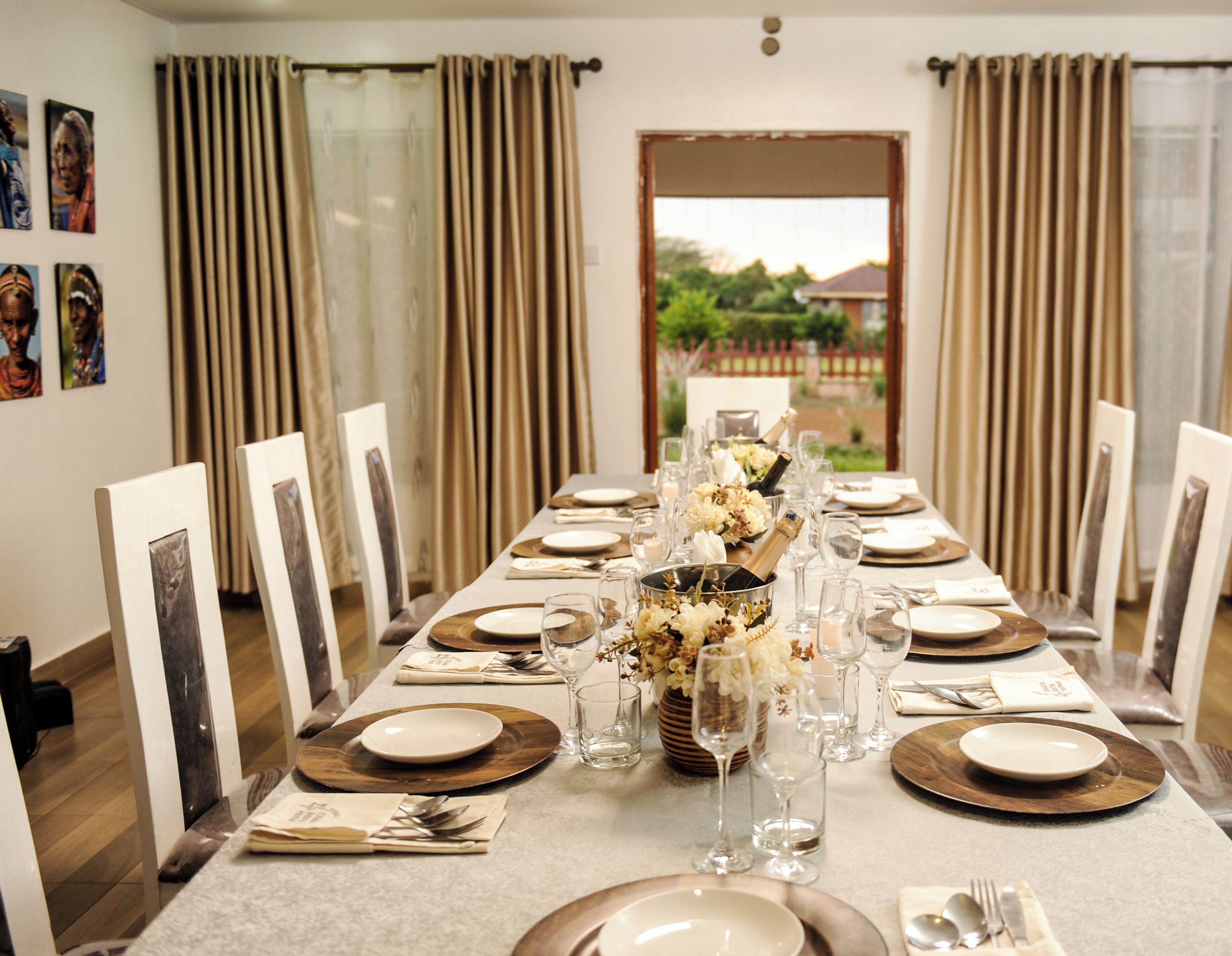 Uma sala de jantar com uma mesa longa posta para refeição, com um vaso de flores, copos de vinho e pratos.