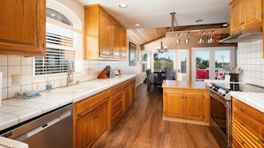 A kitchen with wooden cabinets, a dishwasher, and a dining area with a table and chairs. - Welcome to 'Ocean Oasis' Located on Park Hill in Cambria! (Cambria)