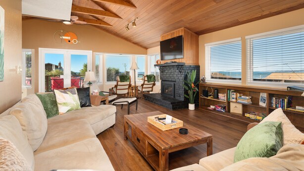 A cozy living room with a fireplace, wooden ceiling beams, comfortable seating, and a bookshelf. - Welcome to 'Ocean Oasis' Located on Park Hill in Cambria! (Cambria)