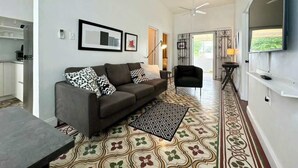Un salon comprenant un canapé, une table basse, un tapis à motifs, un téléviseur et un escalier menant à une autre pièce.