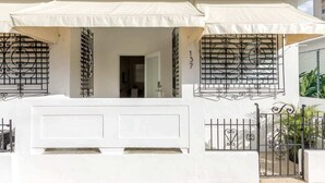 Une maison blanche avec un balcon, des auvents blancs et des portails en fer forgé noir.