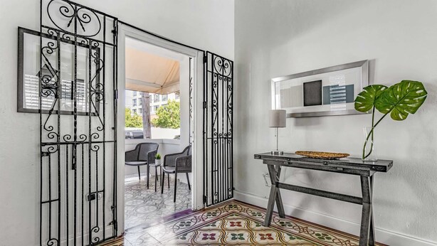 Un couloir avec un sol à motifs, une grille en métal, une table avec une plante et un tableau encadré au mur.