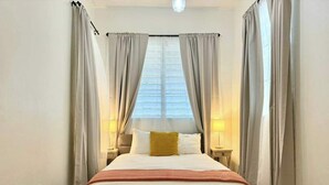 Une chambre d’hôtel avec un grand lit, des rideaux, une table de chevet avec une lampe et un banc en bois.