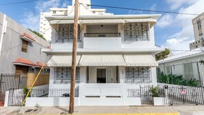 Un immeuble de deux étages avec une façade blanche, des balcons dotés de rampes en métal et une entrée fermée par un portail.