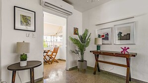 Une chambre d’hôtel moderne avec un plancher en bois, une table ronde avec une lampe, une plante en pot et une console en bois agrémentée d’un objet décoratif.