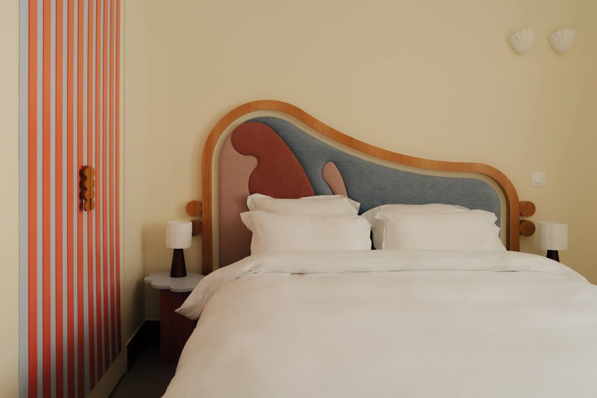 A neatly made bed with a wooden headboard, a bedside table, and a wall with vertical stripes.