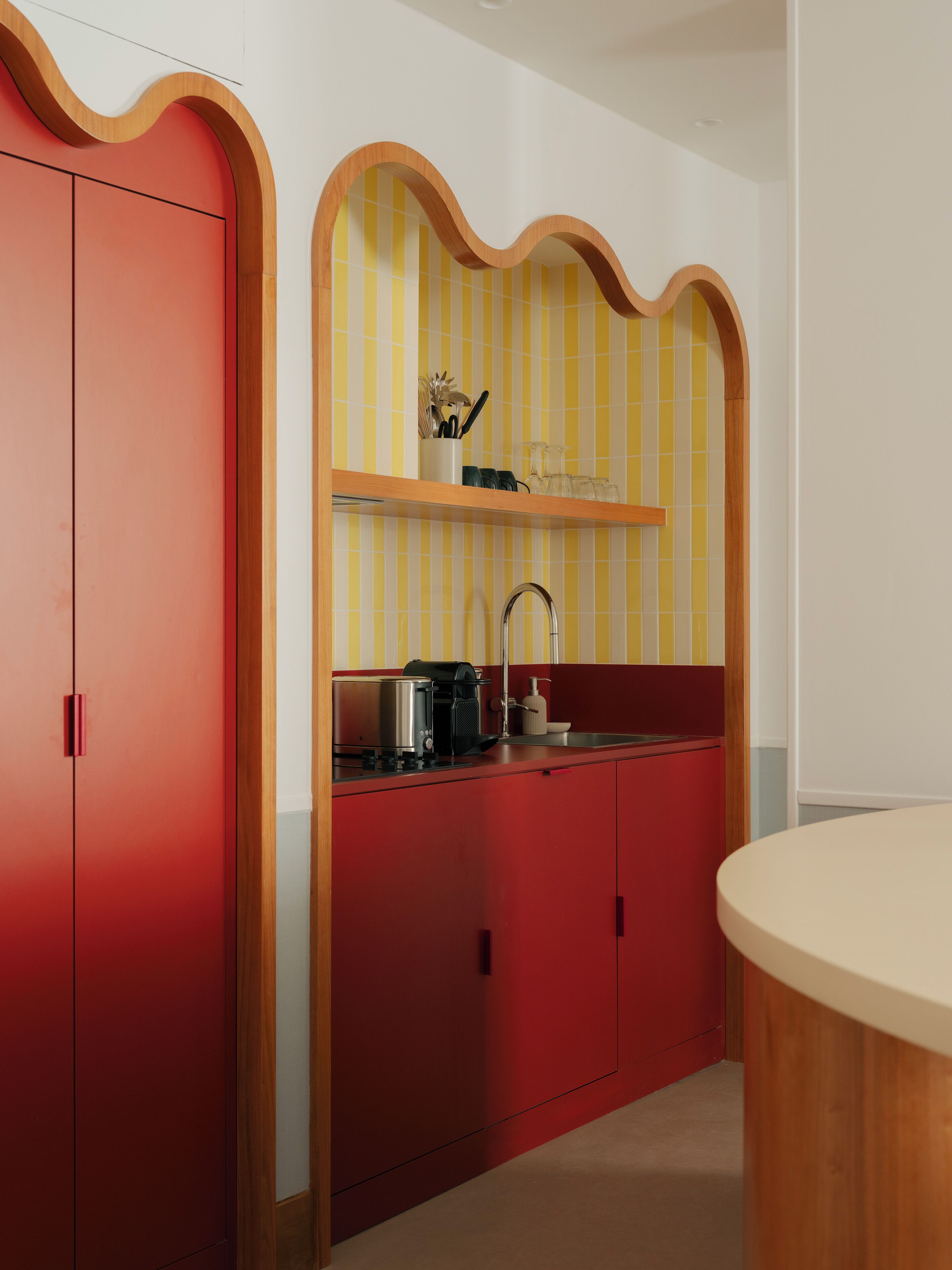 A compact kitchen with a red countertop, a sink, and a wooden shelf above it.