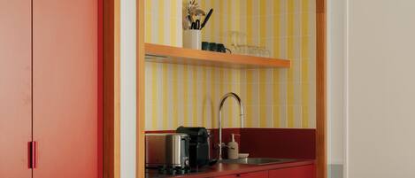 A compact kitchen with a red countertop, a sink, and a wooden shelf above it.