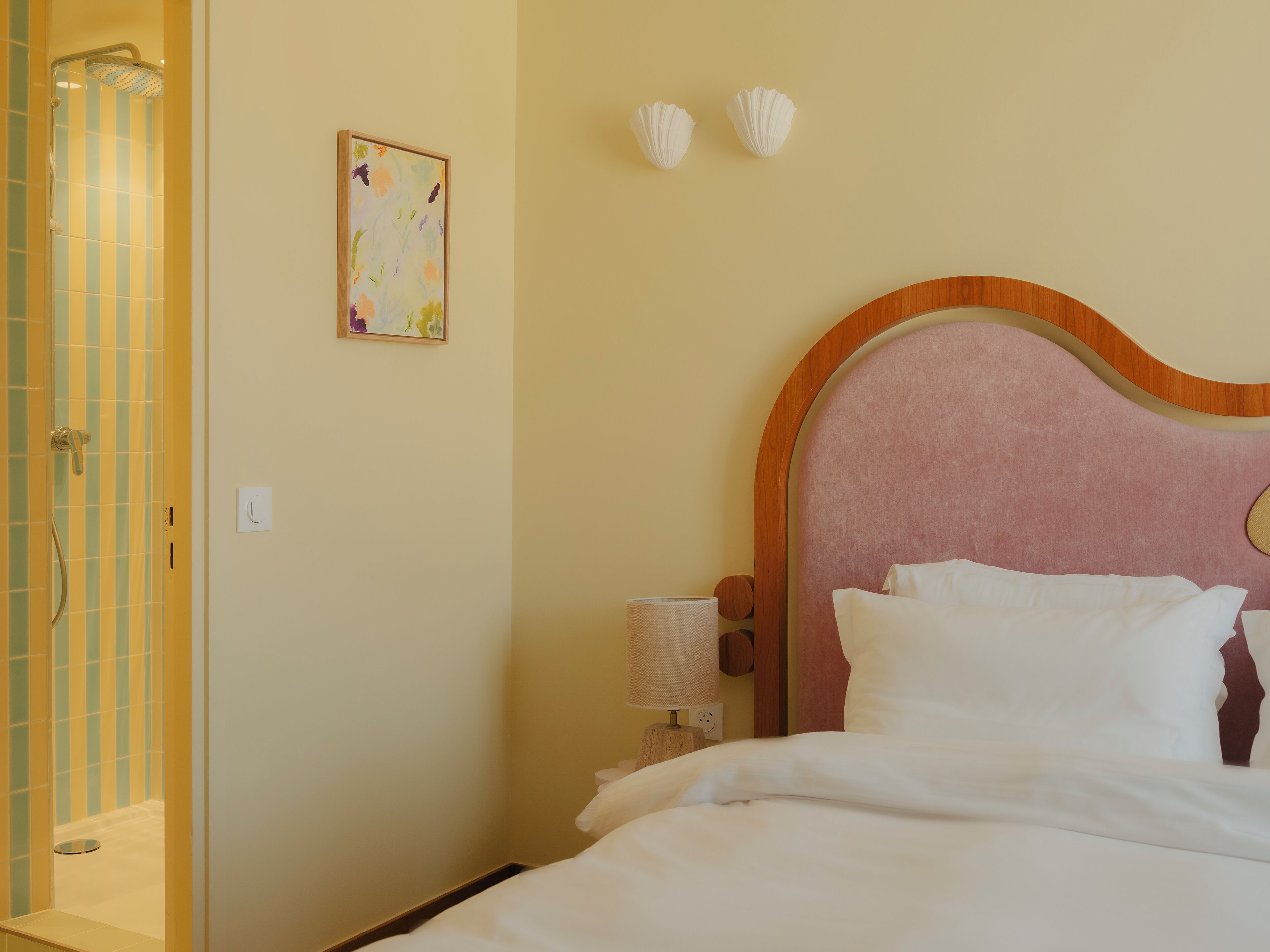 A hotel room with a bed, a shower, and a painting on the wall.