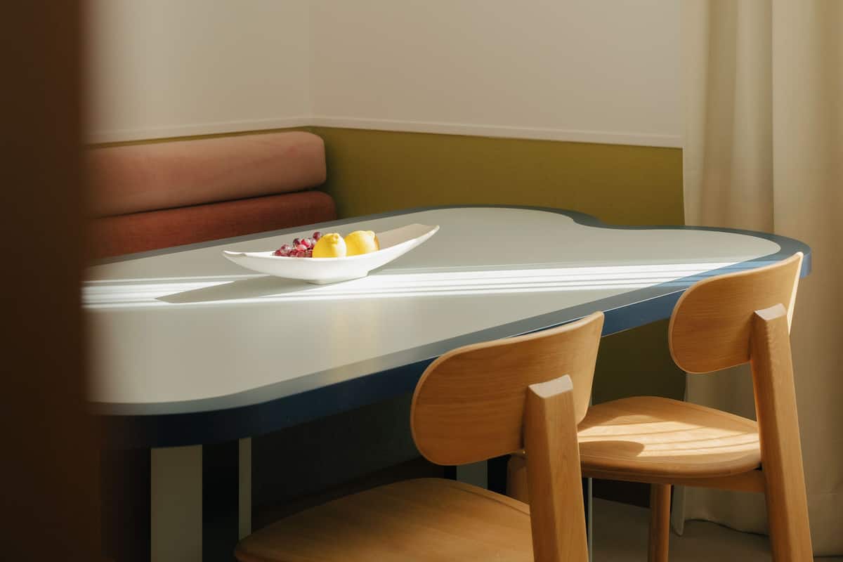 A dining area with a table, chairs, a bench, a framed picture, and a bowl of fruit.