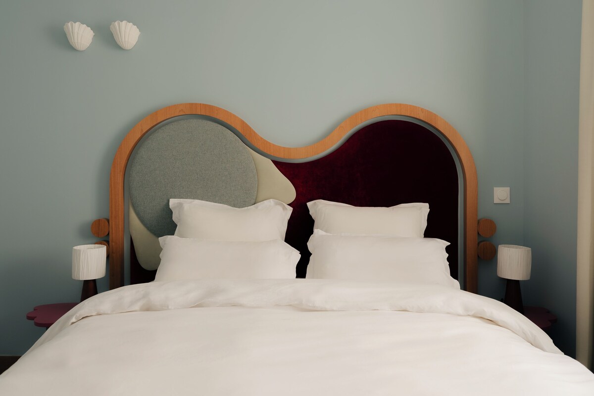 A bed with a unique headboard design, a bedside table, and a wall-mounted light fixture.