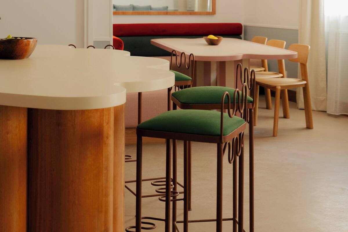 A dining area with a wooden table, green upholstered chairs, and a red bench.