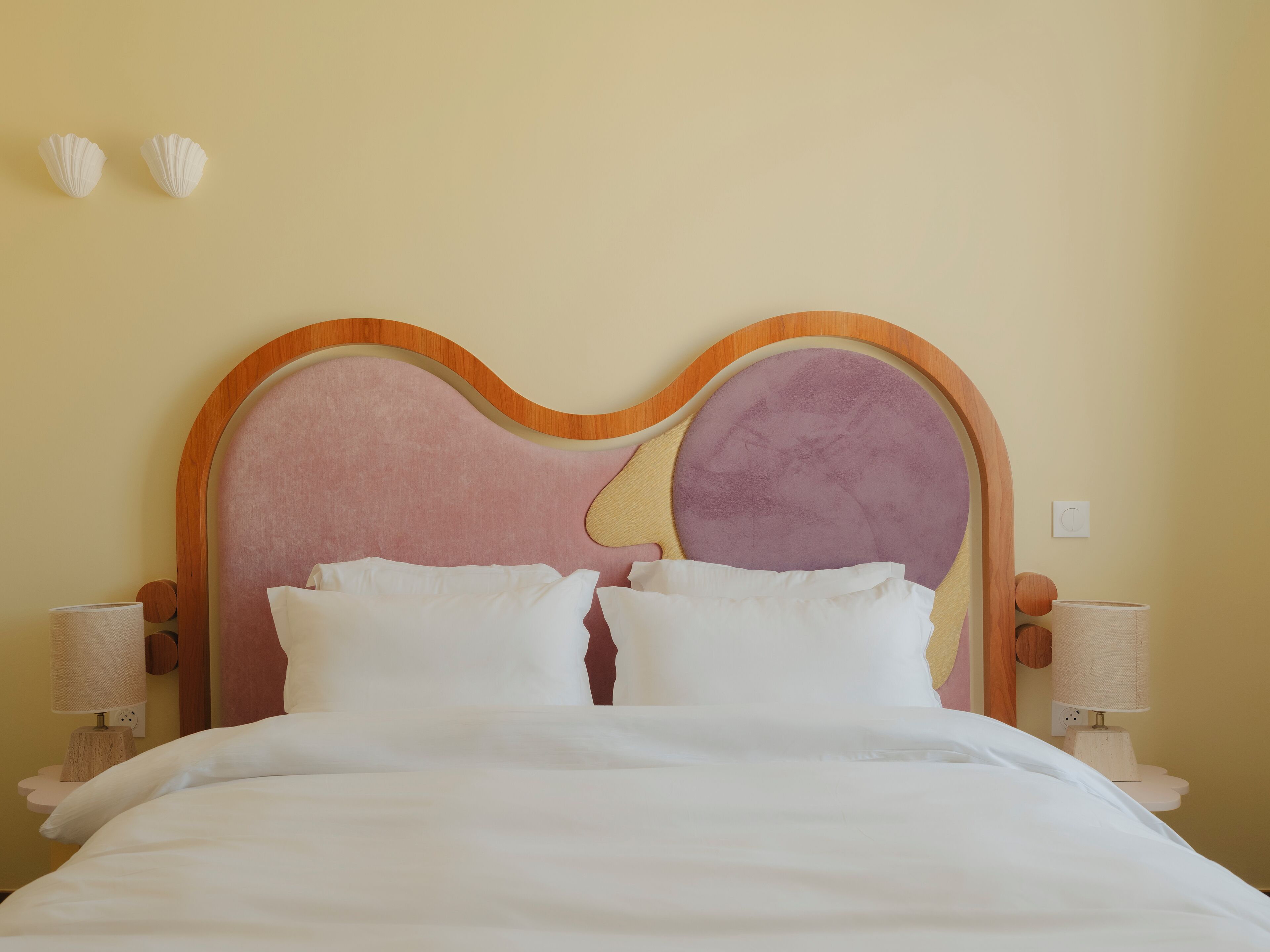A bed with a wooden headboard, two bedside tables with lamps, and a wall-mounted light switch.