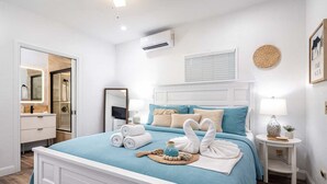 A neatly arranged bedroom with a bed, bedside tables, a mirror, and a wall-mounted air conditioner. - Southwinds Beach House • Jacuzzi • Sleeps 8 (Hollywood)