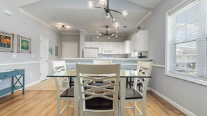 Un coin repas avec une table en verre et des chaises blanches, une cuisine avec des meubles blancs et un luminaire au plafond.