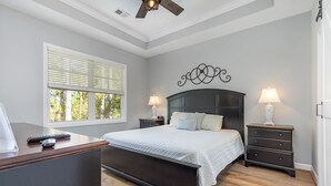 Une chambre à coucher comprenant un lit, deux tables de chevet avec des lampes, un bureau et un ventilateur de plafond.