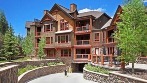 A multi-story lodge with a stone facade, wooden balconies, and a stone retaining wall. - Bluesky 414: Ski-In/Out Peak 9, Private Hot Tub & Fireplace, Shuttle. (Breckenridge)
