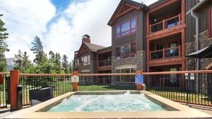 A spa area with a hot tub, stone walls, and a wooden fence. - Bluesky 414: Ski-In/Out Peak 9, Private Hot Tub & Fireplace, Shuttle. (Breckenridge)