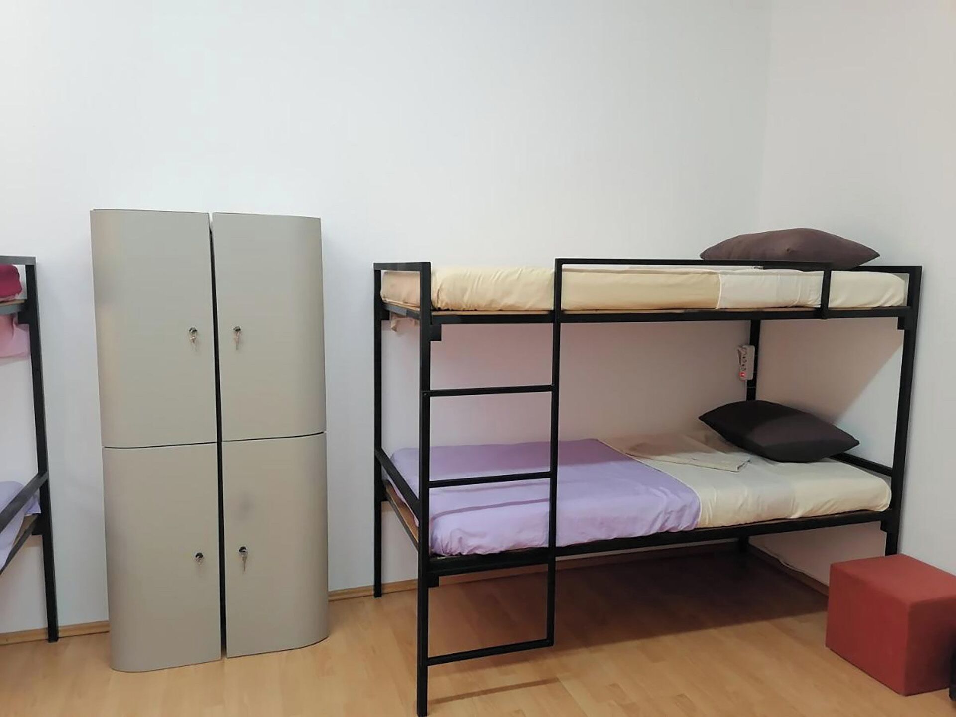 A bunk bed with a wardrobe and a red stool in a room with wooden flooring.