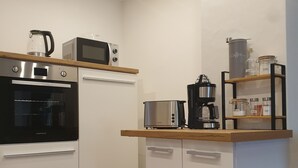 Ett modernt kök med en inbyggd ugn, mikrovågsugn och kaffebryggare, samt en sopbehållare och en behållare för kaffebönor.