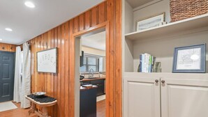 Ein Korridor mit Holzwandverkleidung, einem kleinen Tisch mit einer Schüssel, einem Spiegel und einer Tür zu einer Küchenzeile.