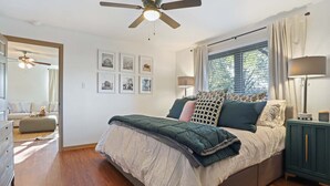 Ein Schlafzimmer mit Bett, Deckenventilator, Fenster mit Vorhängen und einem Schminktisch.