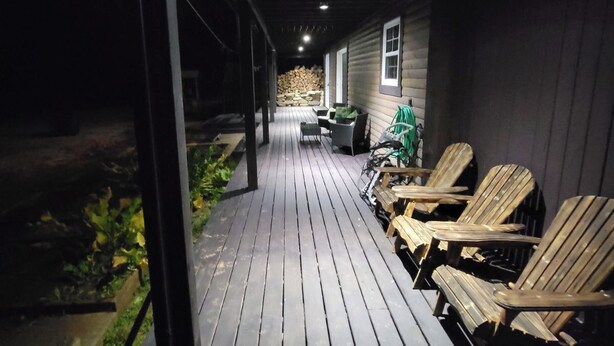 Een overdekt houten terras met stoelen en een tafel, dat leidt naar een gebouw met een raam.
