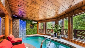 Une piscine intérieure avec un plafond et des murs en bois, des fauteuils rouges et une vue sur la verdure environnante.