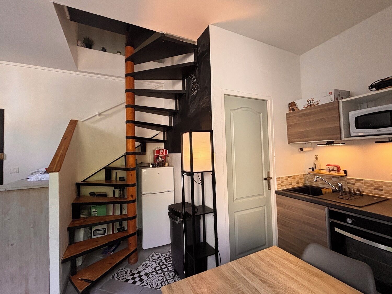 A compact kitchen with a built-in microwave, a small sink, and a wooden dining table.