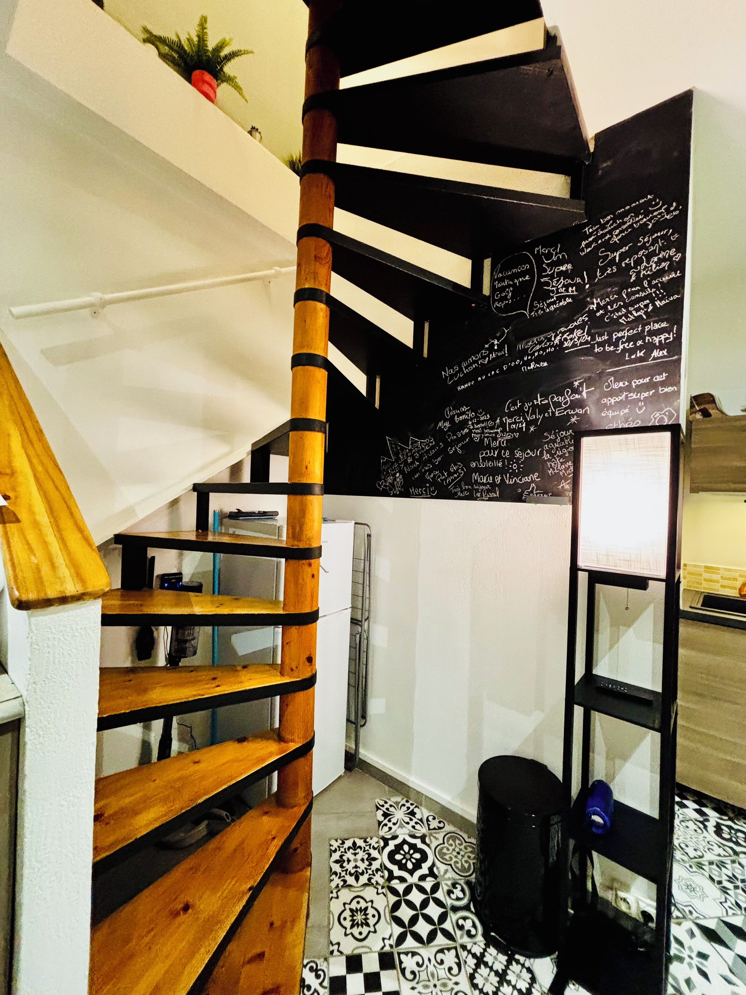 A staircase with wooden steps and black railings, leading to a room with a blackboard filled with writing.
