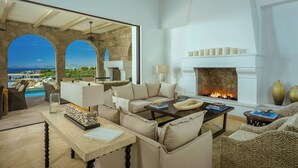 A spacious living room with a stone fireplace, comfortable seating, and a view of the ocean.