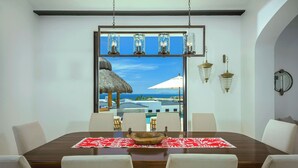 A dining area with a wooden table, white chairs, and a red patterned table runner.