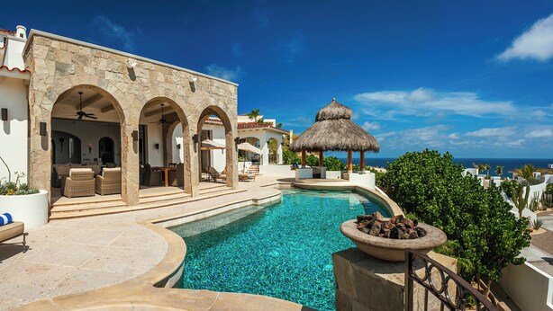 A poolside area with a stone building, outdoor seating, and a thatched-roof structure.
