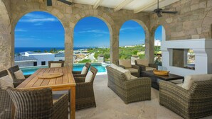 A covered outdoor seating area with stone arches, a pool, and a view of the ocean.