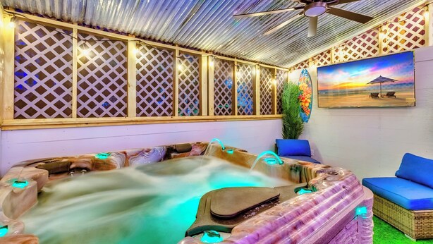 A spa area with a hot tub, blue cushioned seating, a ceiling fan, and a painting of a beach scene. - Raised Beach house/Golf Cart/Hot tub/Arcade/BAR/Pool table (Myrtle Beach)
