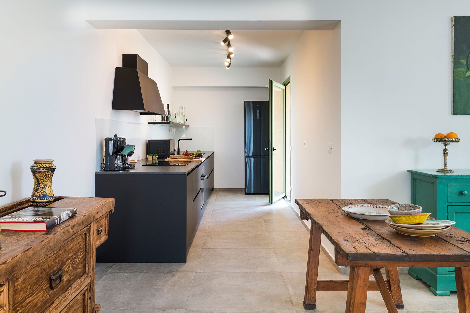 A modern kitchen with a central island, a dining table, and a teal cabinet.