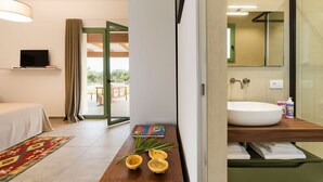A modern hotel room with a bed, a TV, a wooden side table with books and a plant, a large window, and a bathroom with a sink and mirror. - Villa with Pool and A/C in Sicily (Menfi)