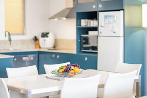 A modern kitchen with a dining table set for two, a refrigerator, and a toaster. - Modern 2 Bedroom, 2 Bath Apartment with ocean views (AIRLIE BEACH)