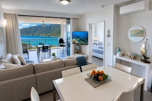 A modern living room with a sofa, dining table, and a balcony with a view of a lake.