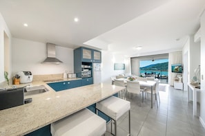 A modern kitchen with a large island, bar stools, and a dining area with a view.