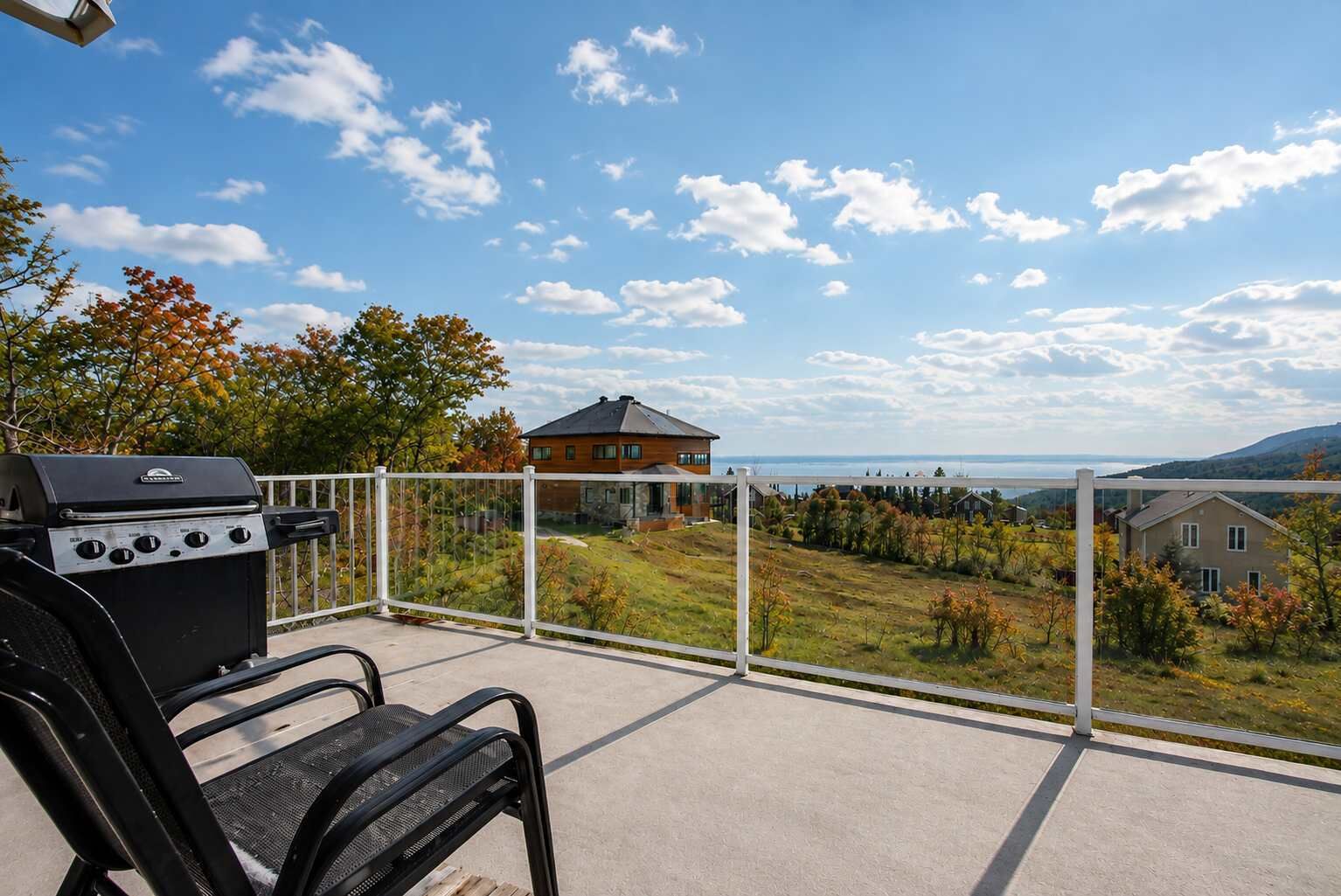 A balcony with a grill, a chair, and a view of houses and a body of water.
