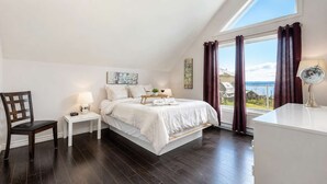 A bedroom with a large bed, a bedside table with a lamp, a chair, and a view of the outdoors through a window. - Spa and River View | Le Haut-Perche (Petite-Rivière-Saint-François)