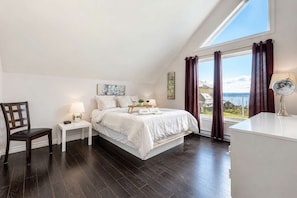 A bedroom with a large bed, a bedside table with a lamp, a chair, and a view of the outdoors through a window. - Spa and River View | Le Haut-Perche (Petite-Rivière-Saint-François)