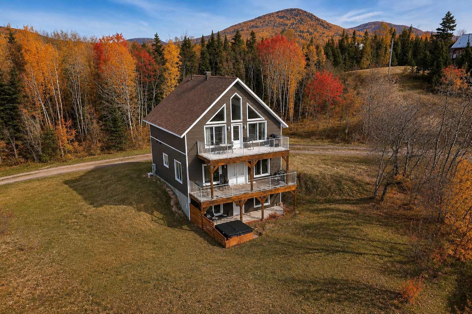 A two-story house with a balcony, surrounded by autumn-colored trees and a hilly landscape.