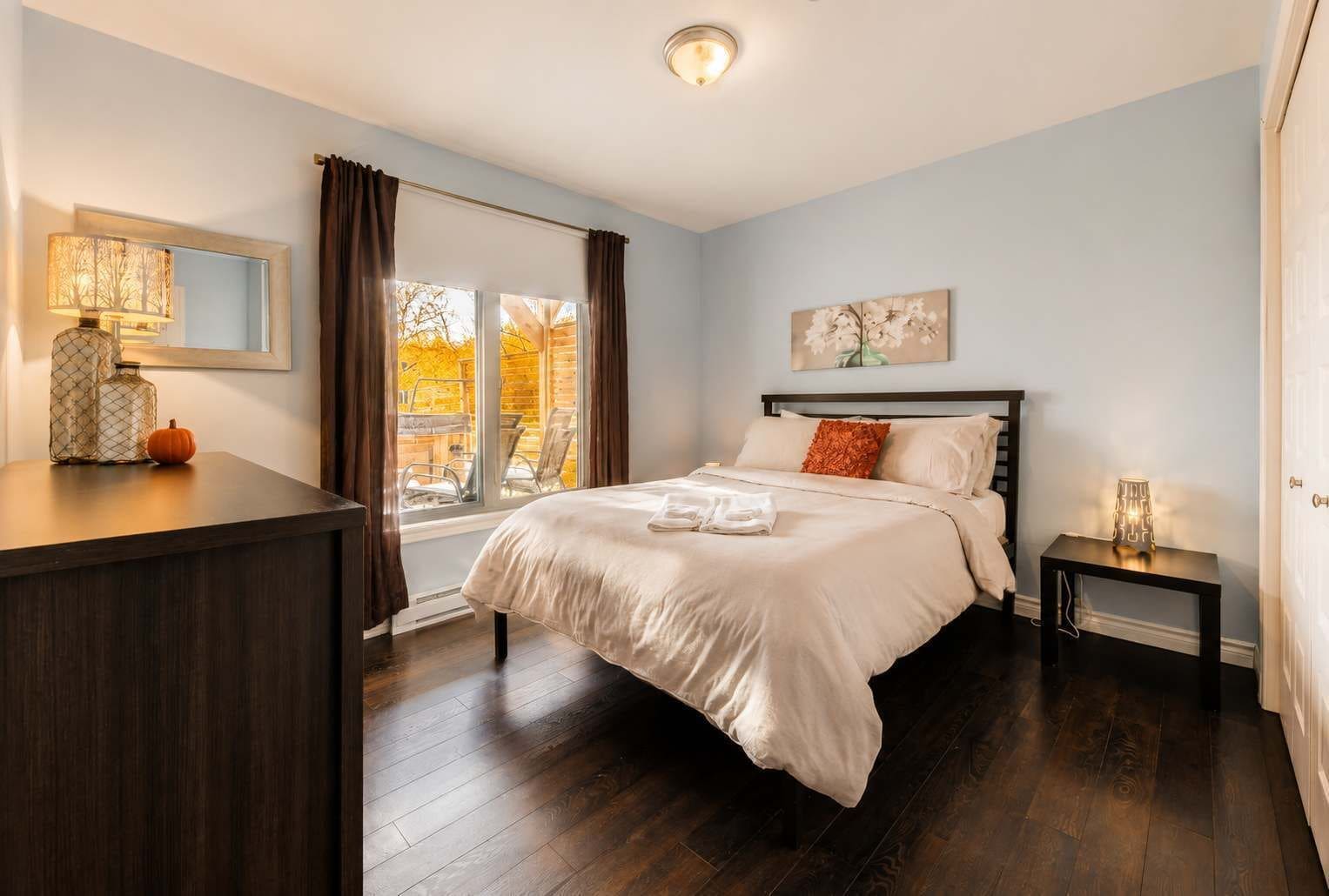 A bedroom with a bed, a nightstand, a lamp, a window with curtains, and a painting on the wall.