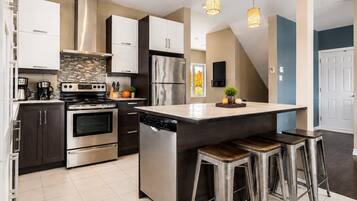 A modern kitchen with stainless steel appliances, a central island with stools, and a dining area.