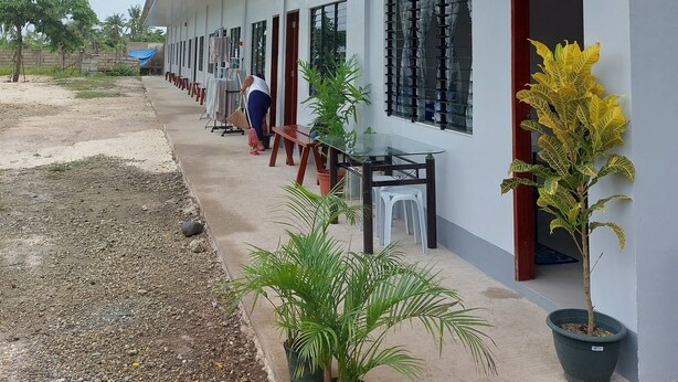 A building with a covered outdoor area, a person sweeping, and potted plants. - LAWAK BAKASYUNAN (Moalboal)
