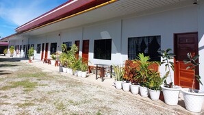 A row of white buildings with red roofs and multiple doors, each with a window. There are potted plants along the walkway. - LAWAK BAKASYUNAN (Moalboal)
