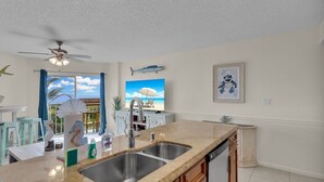 A kitchen with a large island, stainless steel sink, and a ceiling fan.